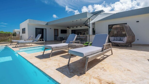 Un espace piscine extérieur moderne, doté de chaises longues et d’un fauteuil en osier.
