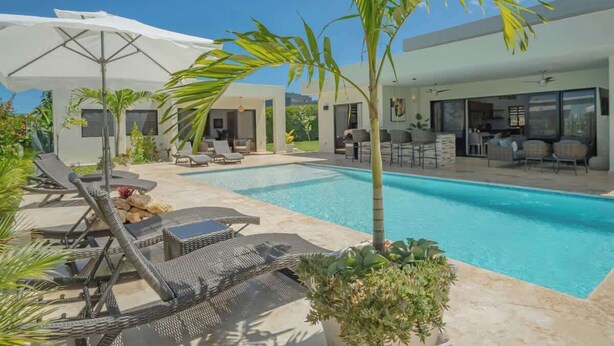 Et moderne poolområde med liggestole, en hvid parasol og en klar, blå pool.