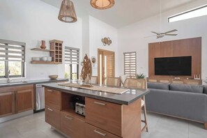 A modern kitchen with wooden cabinets, a central island, and a built-in oven. - A/C in Living Room • Luxury • Guest House. (Sosúa)