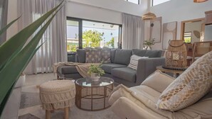 En moderne stue med sofa, rundt sofabord og et stort vindue med gardiner.