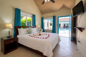 A hotel room with a bed, two bedside lamps, a TV, and a view of the outside. - Courtyard Pool Estate · 6 Suites · Infinity Edge · Casa Linda Sosúa (Sosúa)