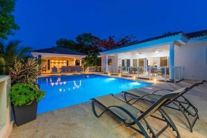 A swimming pool with lounge chairs, a covered patio area, and a building with large windows. - Ocean View Luxe Retreat • 4BR • Pool & Serenity (Sosúa)