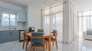 Eine moderne Küche mit Essbereich, Deckenventilator und großen Fenstern mit durchsichtigen Vorhängen.