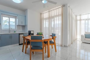 Eine moderne Küche mit Essbereich, Deckenventilator und großen Fenstern mit durchsichtigen Vorhängen.