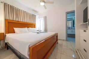 Ein Hotelzimmer mit einem hölzernen Bett, einem Deckenventilator, einem Fernseher und einem durch eine offene Tür einsehbaren Badezimmer.