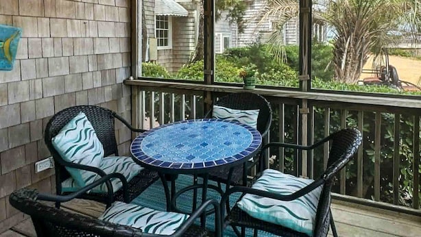 A covered patio with wicker furniture and a mosaic table, overlooking a residential area.