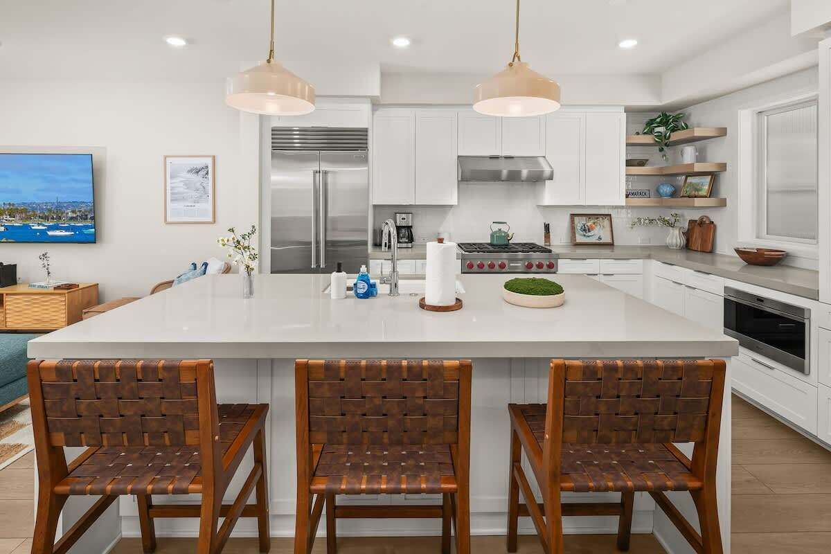 Una cocina moderna con armarios blancos, una isla grande con taburetes de bar, electrodomésticos de acero inoxidable e iluminación colgante.