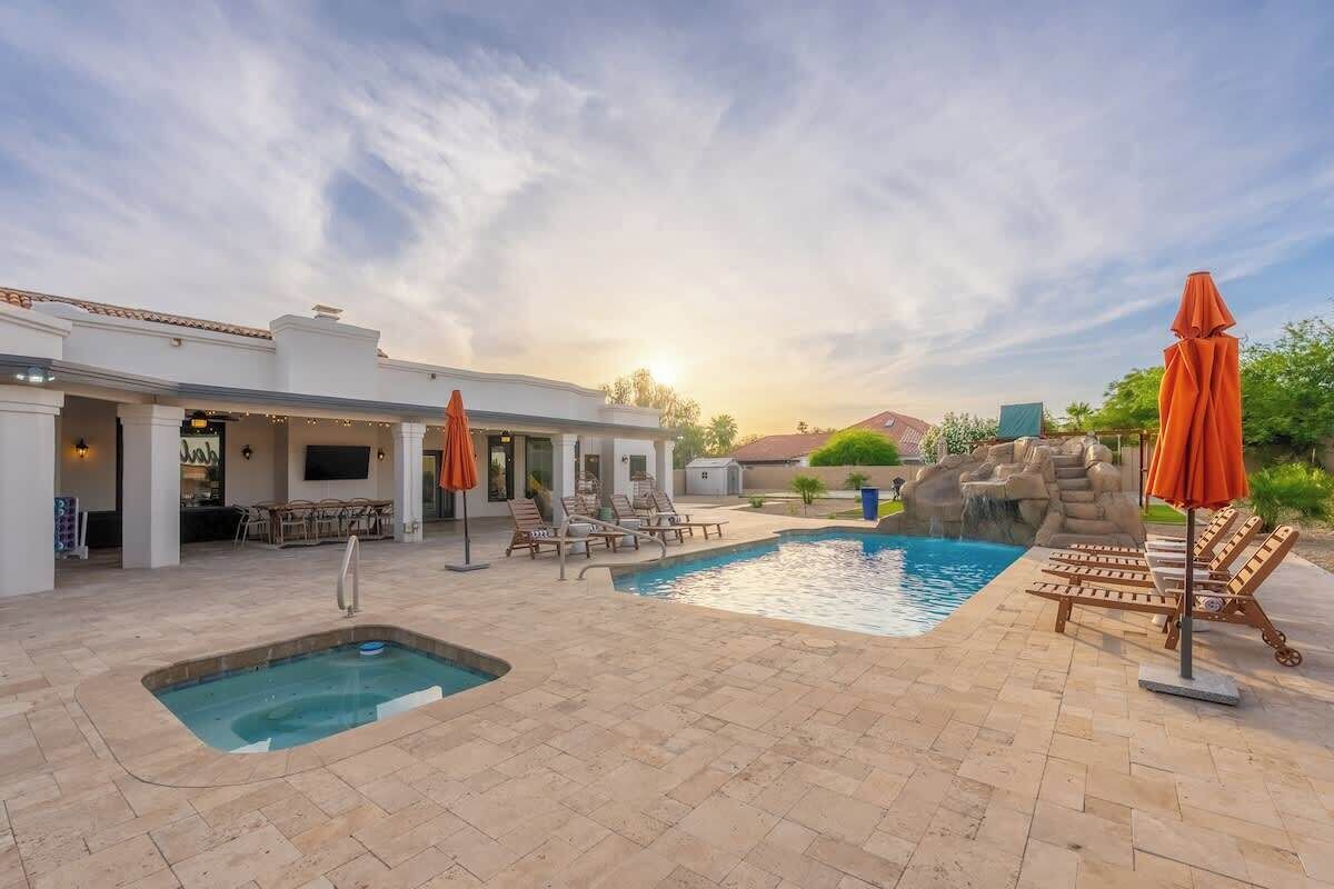 A pool area with lounge chairs and umbrellas, a hot tub, and a patio with outdoor seating.