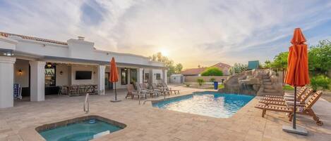 A pool area with lounge chairs and umbrellas, a hot tub, and a patio with outdoor seating.
