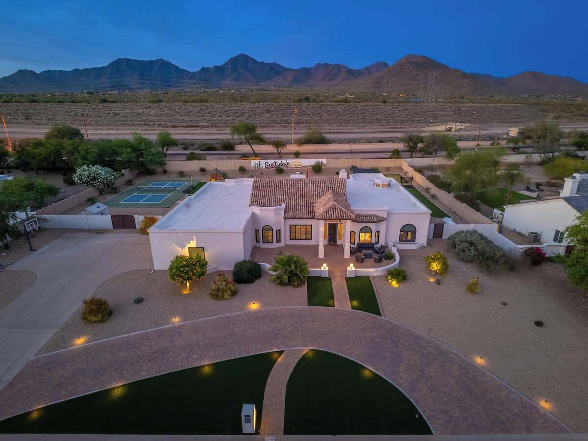 A large house with a patio, a swimming pool, and a tennis court.