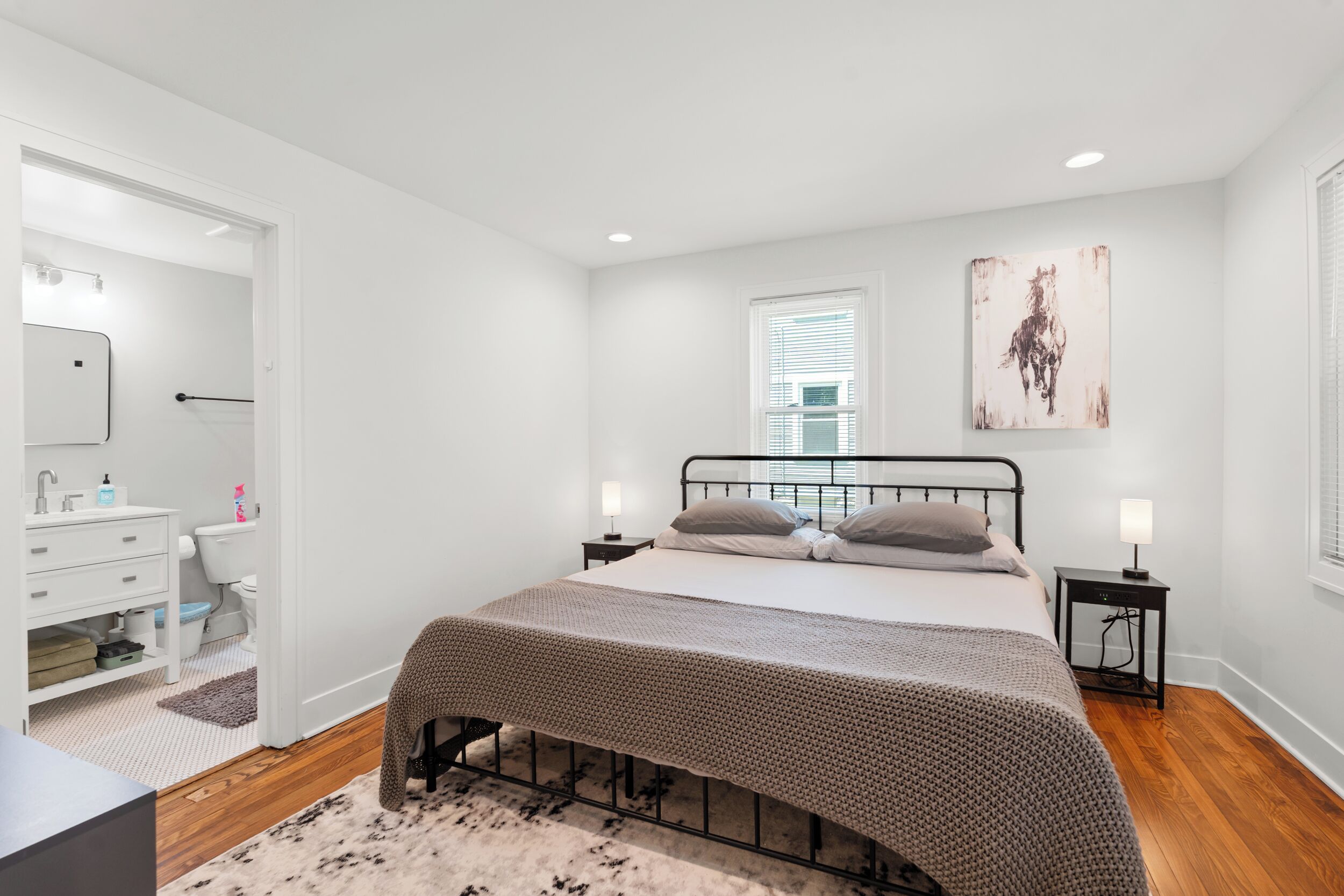A bedroom with a bed, bedside tables, a window, and a bathroom visible through an open door.