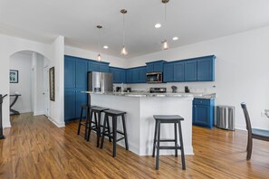 A modern kitchen with blue cabinets, stainless steel appliances, and a central island with stools. - 4BR Home Near MarshWalk + Pro Golf Simulator (Murrells Inlet)
