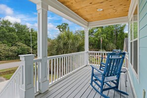 A covered porch with a wooden ceiling, white railings, and a blue rocking chair. - 4BR Home Near MarshWalk + Pro Golf Simulator (Murrells Inlet)