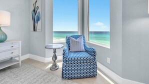 Ein Zimmer mit Blick auf den Ozean, ein blaues Musterstuhl, ein weißer Nachttisch und ein kleiner Tisch.