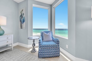 Ein Zimmer mit Blick auf den Ozean, ein blaues Musterstuhl, ein weißer Nachttisch und ein kleiner Tisch.