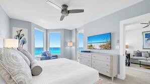 Ein Schlafzimmer mit Bett, Deckenventilator, Fernseher, Kommode und Meerblick.