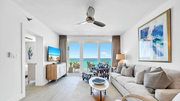 Ein modernes Wohnzimmer mit Deckenventilator, einer Couch, einem Couchtisch und Blick auf den Ozean.