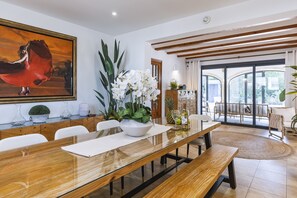 Un coin repas avec une table en bois, des chaises blanches, un grand tableau et une plante en pot.