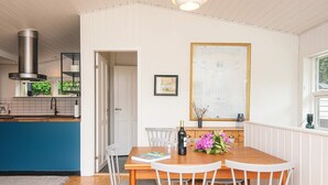 Un coin repas avec une table en bois, des chaises blanches, une bouteille de vin et une œuvre d’art encadrée accrochée au mur.