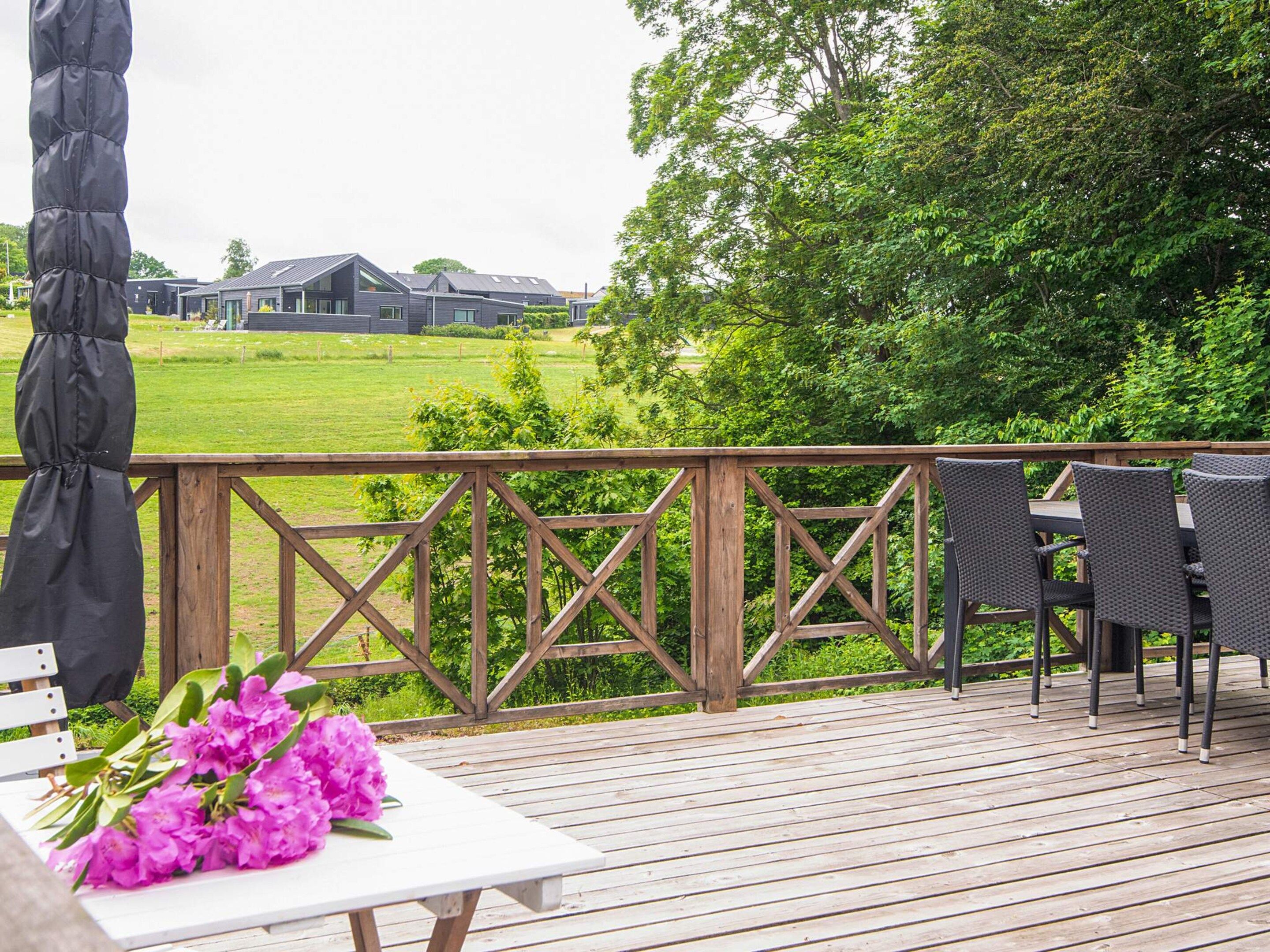 A wooden deck with a table and chairs, overlooking a grassy area with buildings in the distance.