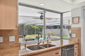 Eine Küche mit großem Fenster, Deckenventilator und Blick auf einen Garten.