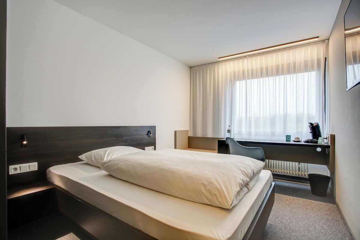 A modern hotel room with a bed, desk, and window with curtains.
