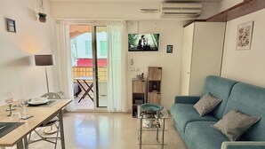 Un salon avec un canapé bleu, une table basse en verre, une table à manger avec des chaises, un téléviseur fixé au mur et une porte-fenêtre coulissante donnant sur un espace extérieur.