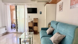 Un salon avec un canapé de couleur turquoise, une table basse en verre et un téléviseur fixé au mur.