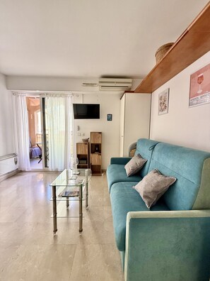 Ein Wohnzimmer mit einem türkisfarbenen Sofa, einem Glastisch und einem Fernseher an der Wand.