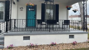 Ein Haus mit einer türkisblauen Tür, schwarzen Fensterläden, einer überdachten Veranda mit Deckenventilator und Sitzgelegenheiten im Freien.