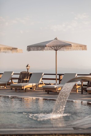 A pool area with lounge chairs and umbrellas, a water feature, and a lamp post.