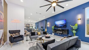 A modern living room with a ceiling fan, a flat-screen TV, and a neon sign. - Melanin Luxe GroupStay Houston NRG Sleeps 14 (Houston)