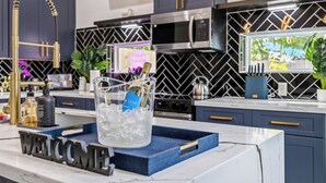 A modern kitchen with dark cabinets, a stainless steel microwave, a gold faucet, and a welcome sign. - Melanin Luxe GroupStay Houston NRG Sleeps 14 (Houston)