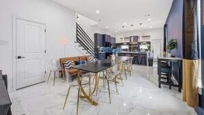 A modern kitchen with dark cabinets, a central island, and a staircase leading to an upper level. - Melanin Luxe GroupStay Houston NRG Sleeps 14 (Houston)