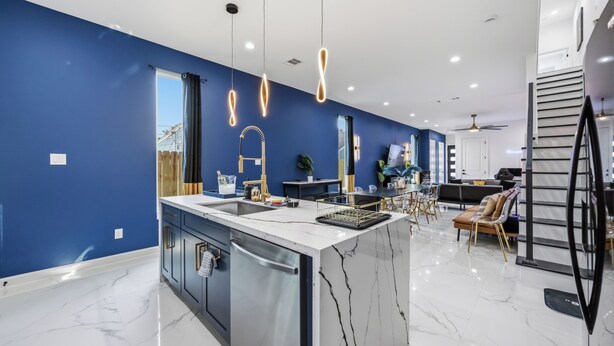 A modern kitchen with a marble island, blue walls, and pendant lighting. - Melanin Luxe GroupStay Houston NRG Sleeps 14 (Houston)