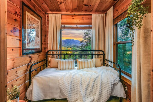 Une chambre dans une cabane en bois, avec un lit, des rideaux et une fenêtre donnant sur les montagnes.