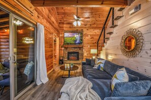 L’intérieur d’une cabane en rondins, avec une cheminée, un téléviseur, un ventilateur de plafond et un coin salon confortable.