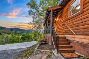 Eine Blockhütte mit Veranda, Treppen und Blick auf die umliegende Landschaft.