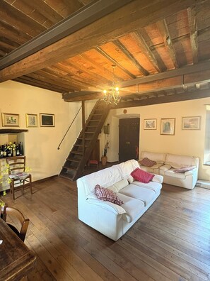Een ruime woonkamer met een houten plafond, een trap en een bank met decoratieve kussens.