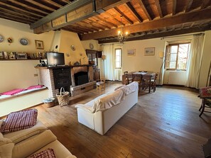 Een woonkamer met een open haard, houten vloeren, een bank, een televisie en een eethoek.