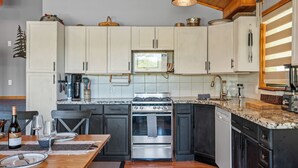 Una cocina con armarios blancos, una estufa de acero inoxidable y un microondas. Hay una mesa de comedor con una botella de vino y copas.