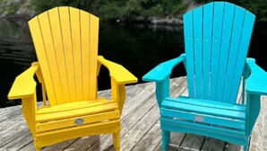 Dos sillas Adirondack sobre un muelle de madera, con un lago rodeado de bosque al fondo.