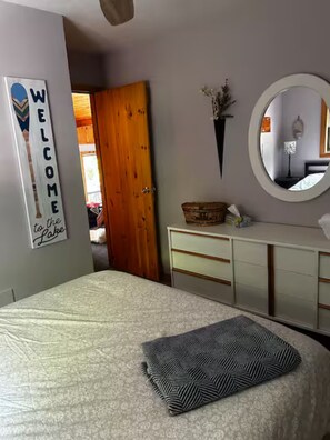 A bedroom with a bed, a dresser, a mirror, and a welcome sign.