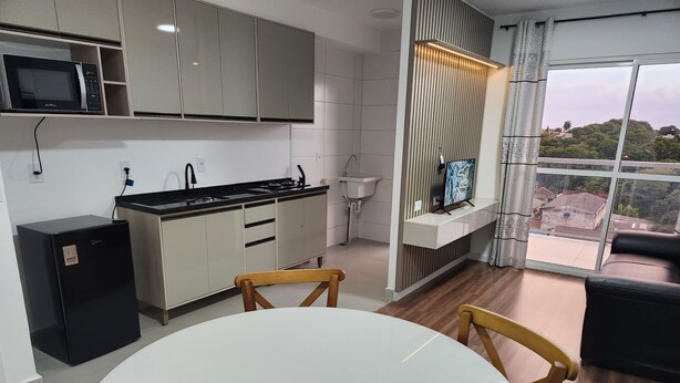 Eine moderne Küche mit Mikrowelle, Herd und Spüle, ein Essbereich mit rundem Tisch und Stühlen sowie ein großes Fenster mit Aussicht.