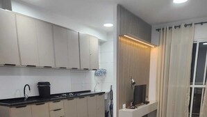 Eine moderne Küche mit weißen Schränken, einer schwarzen Arbeitsplatte und einem eingebauten Herd. Es gibt eine Essecke mit einem runden Tisch und zwei Stühlen.