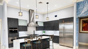A modern kitchen with a central island, stainless steel appliances, pendant lighting, and a marble backsplash.