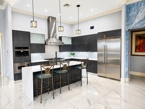Una cocina moderna con una isla central, electrodomésticos de acero inoxidable, iluminación colgante y un salpicadero de mármol.