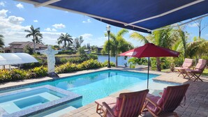 A swimming pool with a tiled deck, lounge chairs, and a red umbrella.
