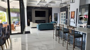 A modern kitchen with a bar area, a dining set, and a living area with a sofa and chairs.