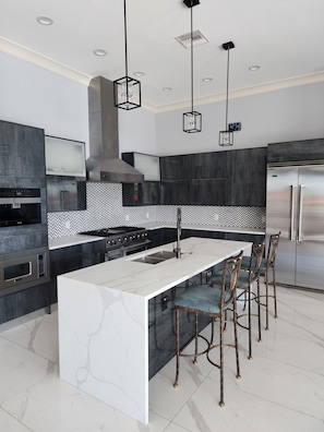 A modern kitchen with a central island, stainless steel appliances, and a herringbone-patterned backsplash.